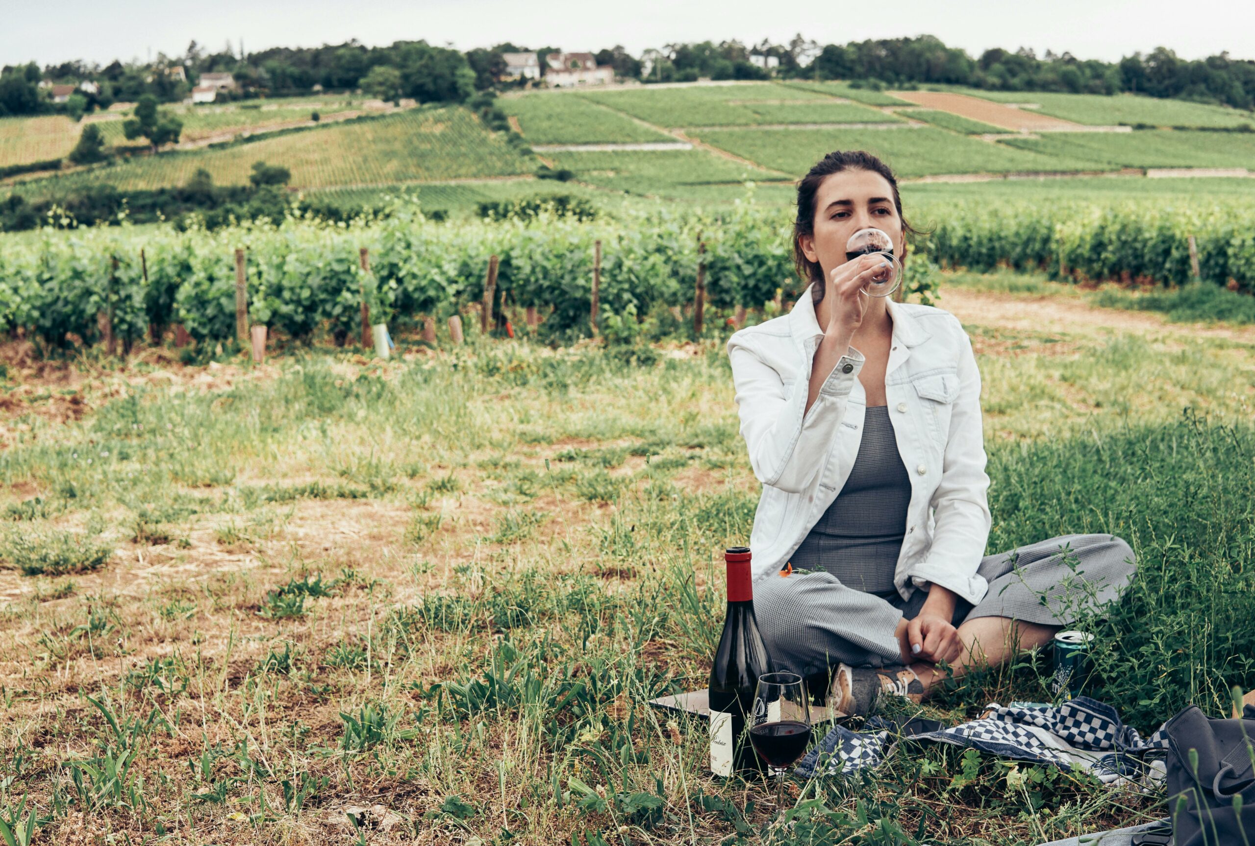 A woman savoring wine in a picturesque vineyard in Bourgogne-Franche-Comté, France.